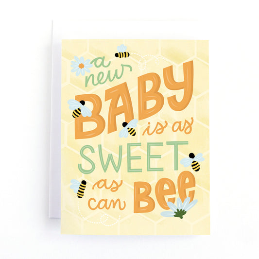 Honey Bee themed baby shower card with playful hand lettering that says, A new baby is as sweet as can bee. Surrounded by bumble bees on a honey comb background.