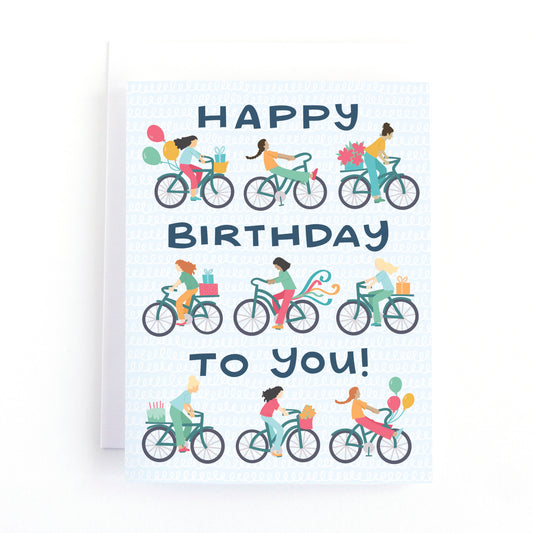 Bike themed birthday card for her with colourful illustrations of girls riding bikes with balloons, streamers and presents and the text, Happy Birthday to You!