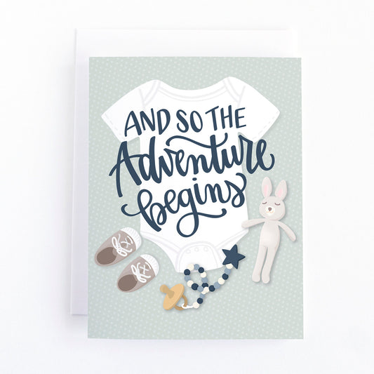 Gender neutral baby shower card with a flat lay of baby layette including a onsie, baby shoes, pacifer and soft toy with the message "and so the adventure begins"