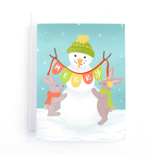 A winter holiday card featuring a snowman and bunnies playing in the snow. the snowman is holding a christmas garland that says Merry
