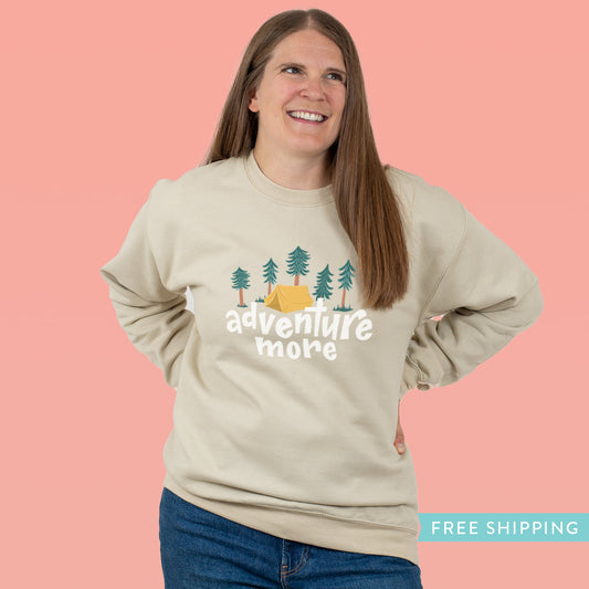 Unisex sweatshirt in a soft sand colour with the hand drawn design on the front that says, Adventure More with and tent surrounded by pine trees.
