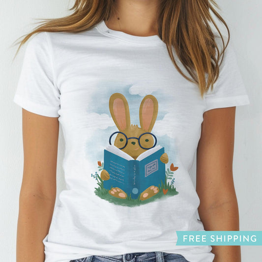 women's white graphic tee featuring a hand drawn illustration of a bunny rabbit reading a book in a field of flowers.