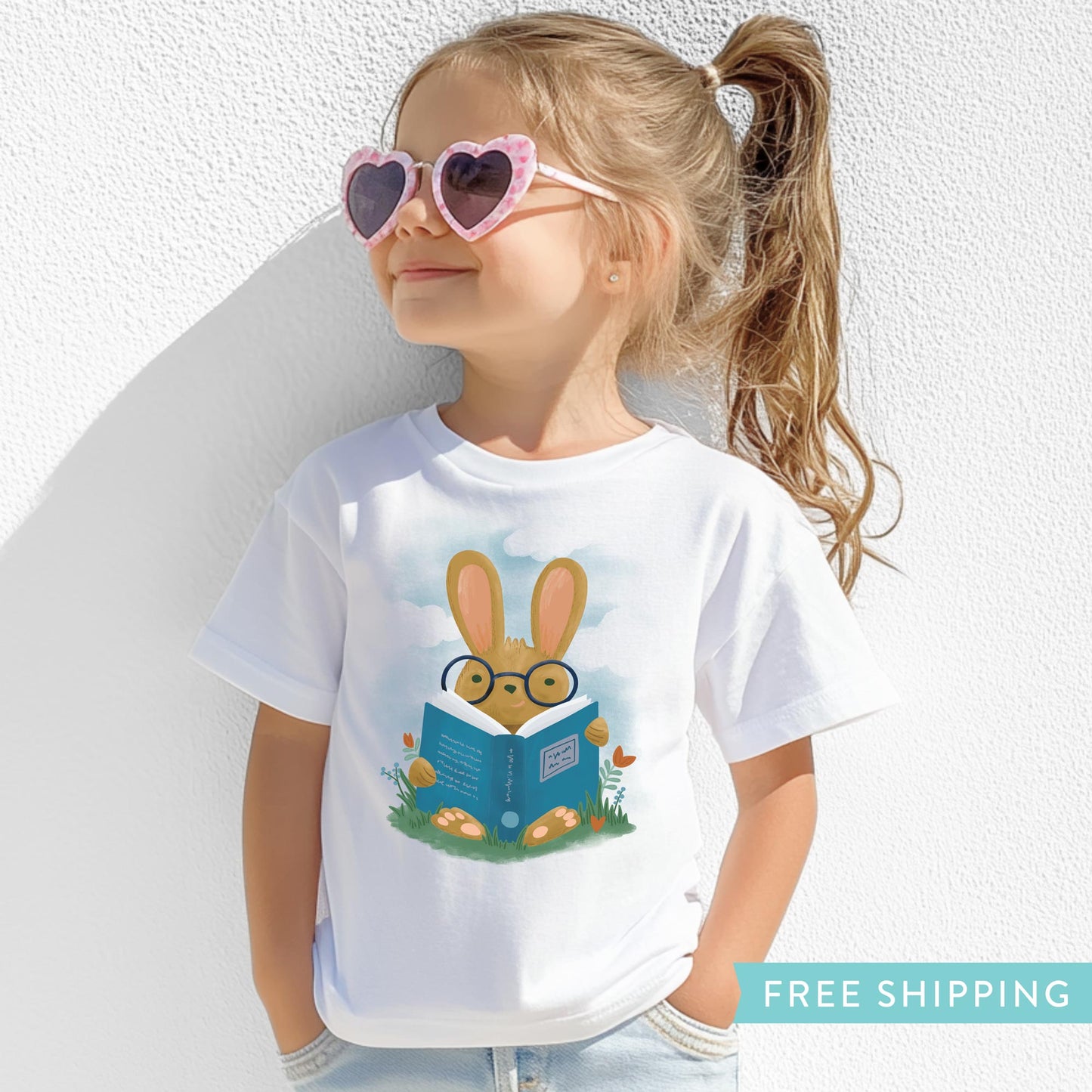 kid's white t-shirt with an illustration of a bunny rabbit reading a book in a field of flowers.