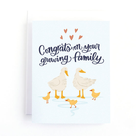 New baby card for parents of twins, triplets and quadruplets featuring a sweet illustration of a mother and father duck with their ducklings and the hand lettered  greeting, congrats on your growing family.