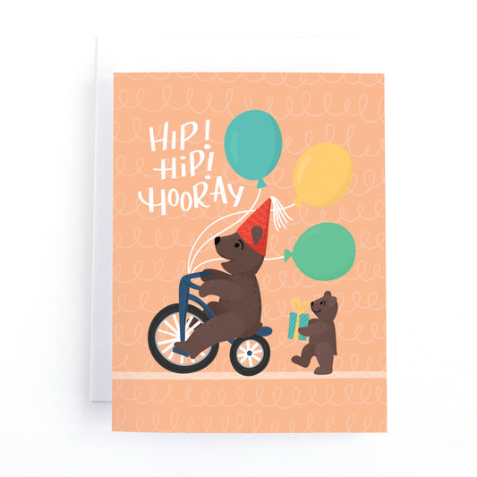Cute kids birthday card with two bears riding a bike and carrying balloons and presents and the text, Hip Hip Hooray.