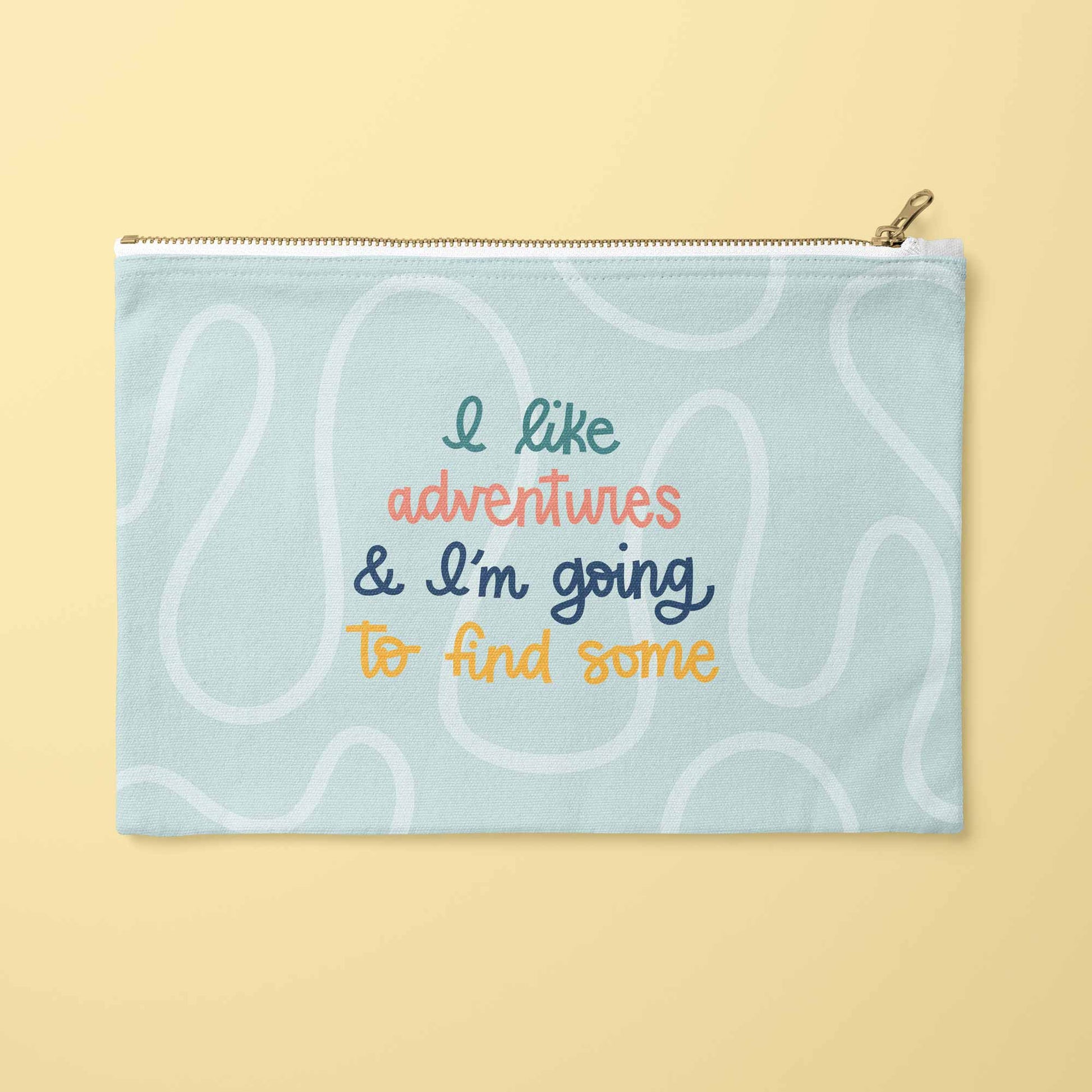 A light blue zippered pouch with a gold zipper and a gold pull tab, featuring a retro-style pattern of wavy white lines and colorful text that reads 'I like adventures & I'm going to find some'. 
