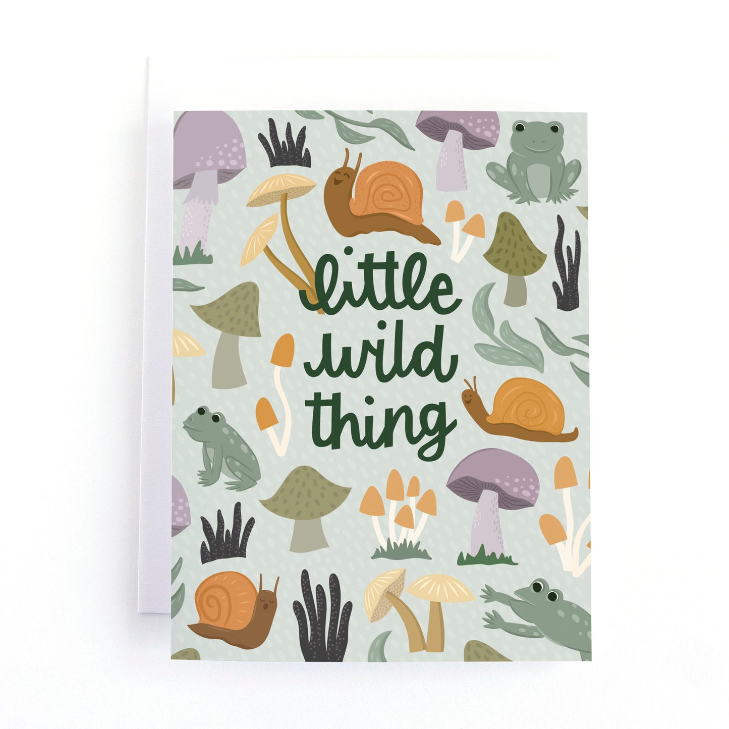 A new baby greeting card with a white envelope, featuring a whimsical forest pattern of snails, mushrooms, and a frog with the text 'little wild thing' in dark green script.