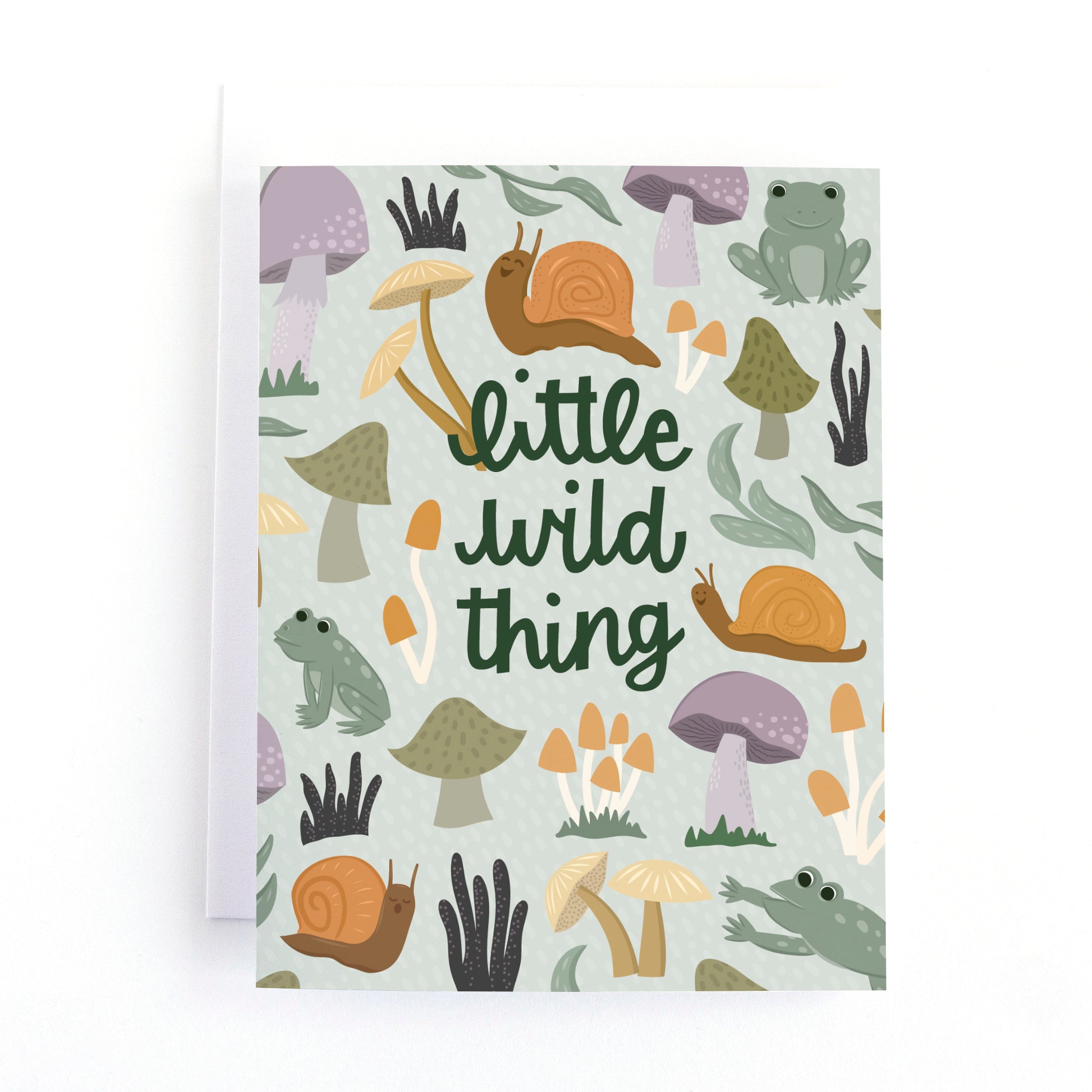A new baby greeting card with a white envelope, featuring a whimsical forest pattern of snails, mushrooms, and a frog with the text 'little wild thing' in dark green script.