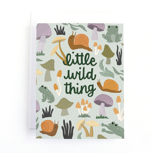 A new baby greeting card with a white envelope, featuring a whimsical forest pattern of snails, mushrooms, and a frog with the text 'little wild thing' in dark green script.