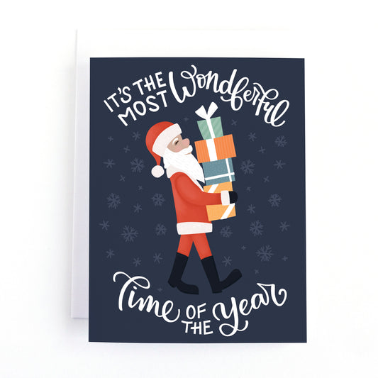 Christmas card with an illustration of santa carrying a stack of gifts and the message it's the most wonderful time of the year.