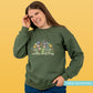 Woman wearing a green sweatshirt with floral design and 'wild and free' text