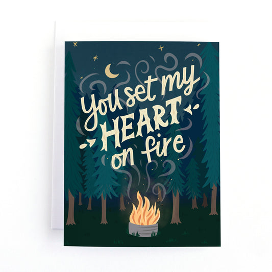Valentine's Day Card with an illustration of a campfire in the woods under a starry sky with the text, you set my heart of fire.