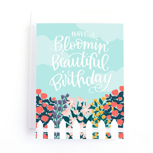 Floral birthday card with a picket fence around a beautiful flower garden and the hand lettered greeting, have a blooming beautiful birthday