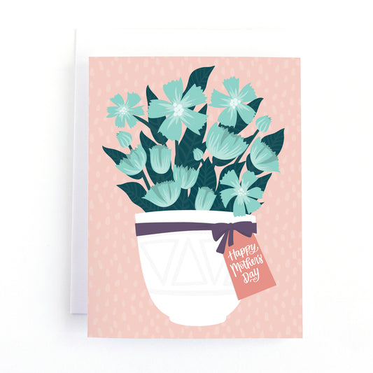 Mother's day card with a white flower pot full of blue flowers and a gift tag tied on with a ribbon that says happy mothers day on a pink background.