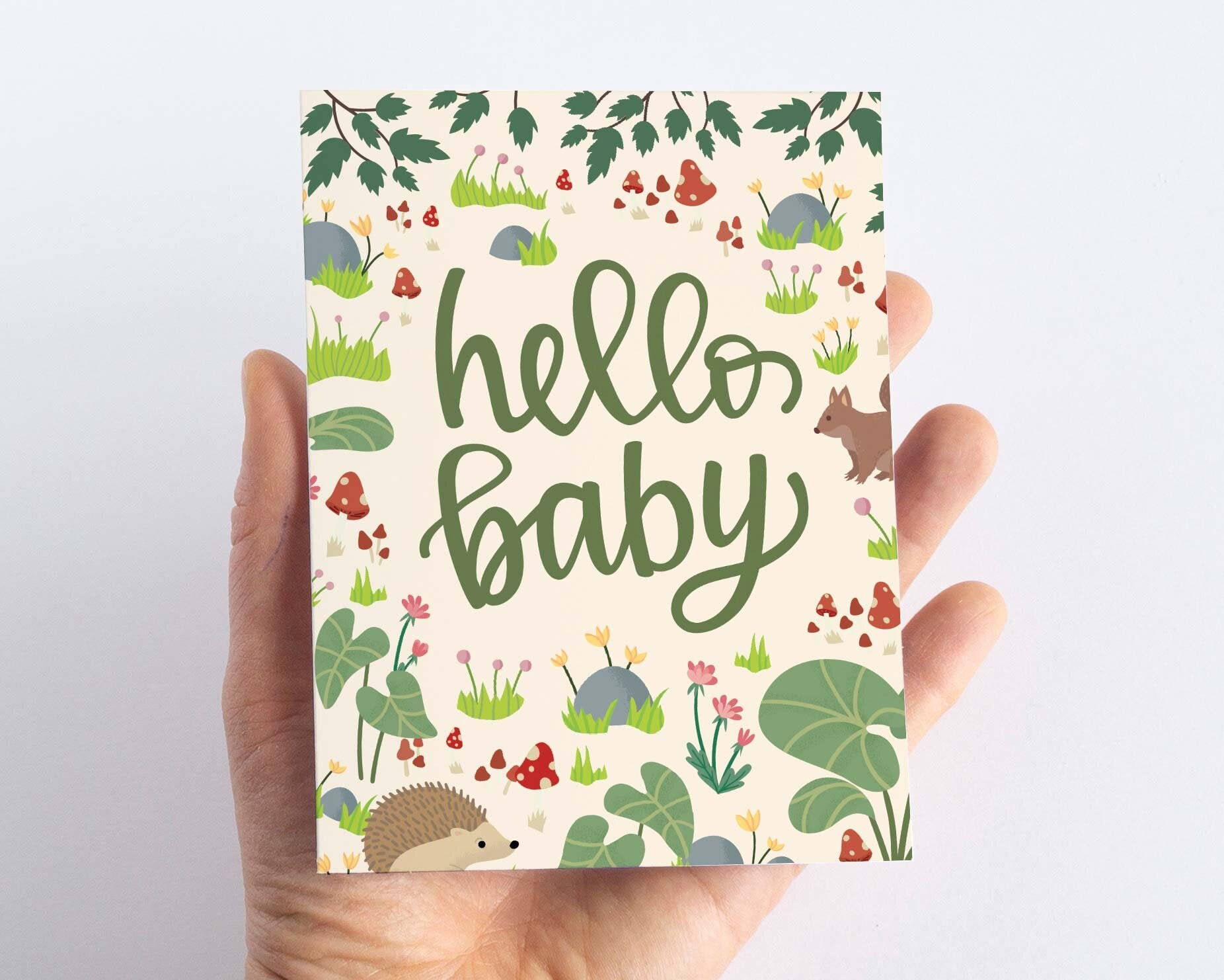 Baby Shower card with woodland forest illustrations including a squirrel, hedgehog and mushrooms and the message hello baby Scale