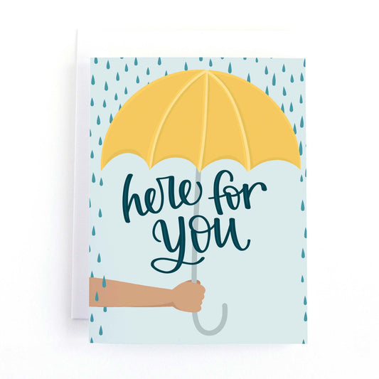 Sympathy and encouragement card with a hand holding a yellow umbrella in a rain storm and the text, Here for you.