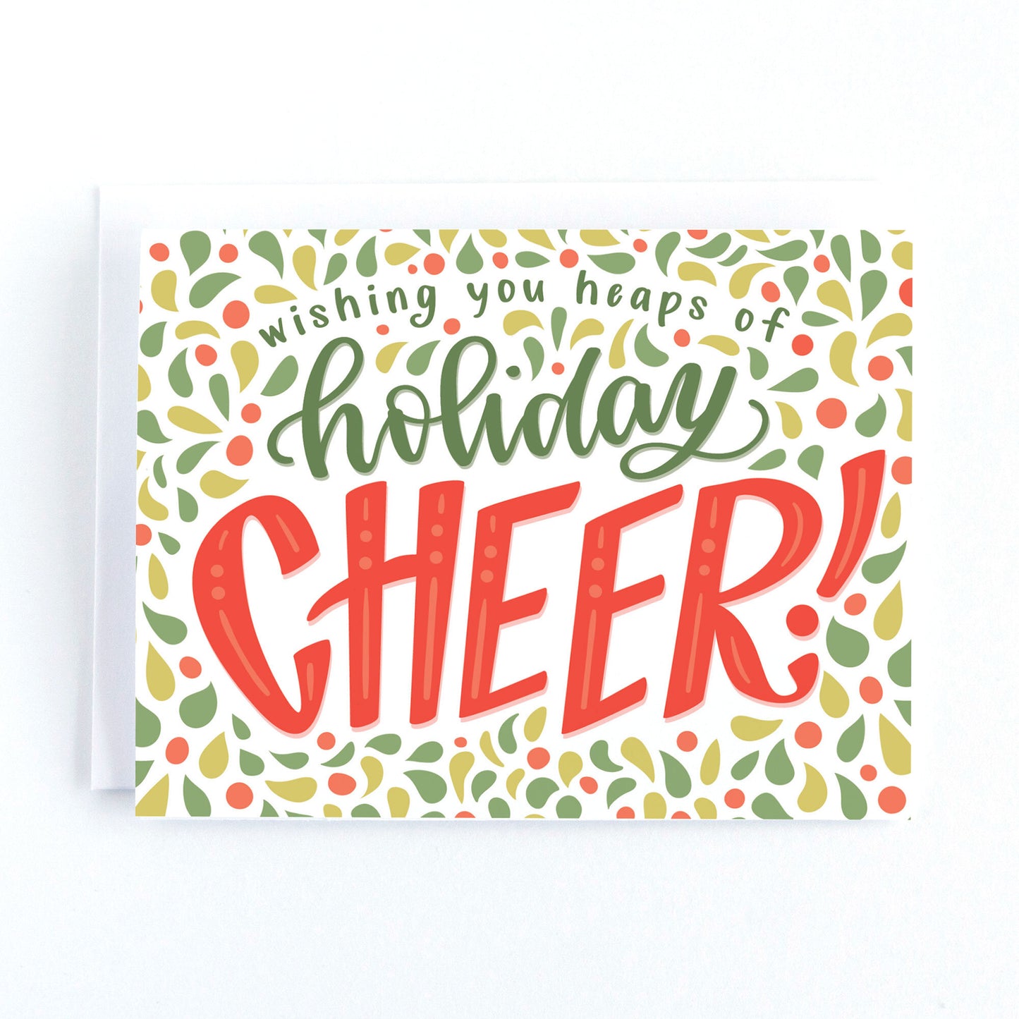 Christmas card featuring playful lettering, and intricate border and text the says, wishing you heaps of holiday cheer in a traditional red and green colour palette.