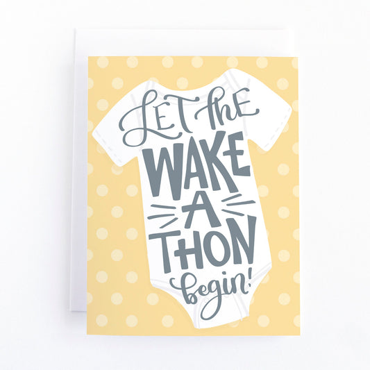 New baby card with a white baby shirt on a yellow background and the funny hand lettered message, "Let the wake a thon begin"