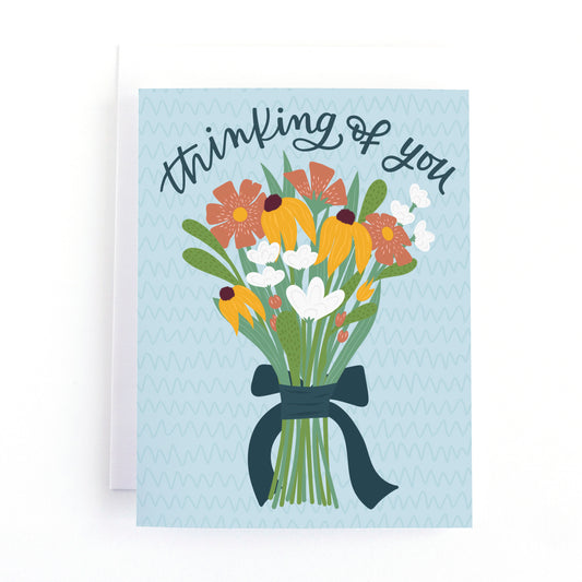 thinking of you card with a simple hand tied bouquet of flowers and the hand lettered text, thinking of you on a textured blue background.